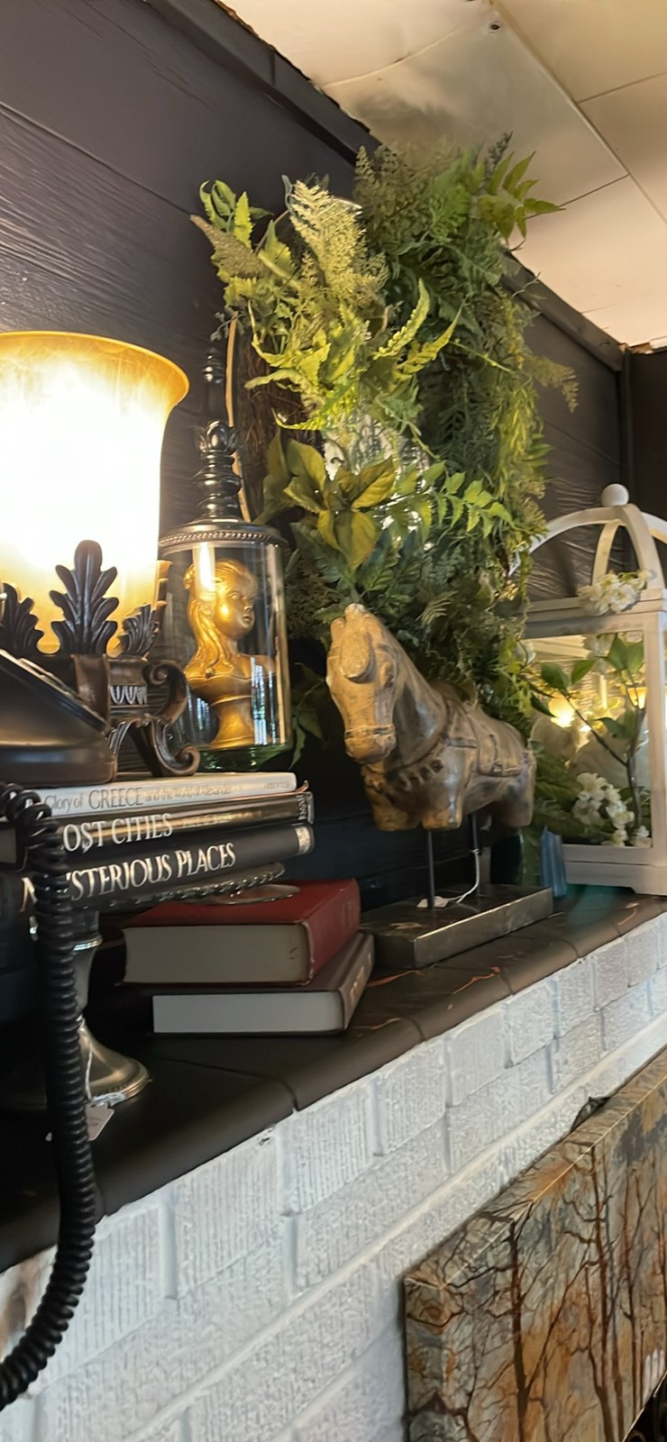 Vintage books, a horse sculpture, a glass display, and greenery on a white brick mantel