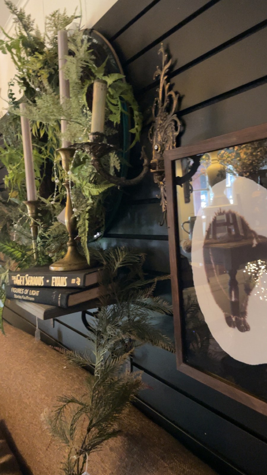 Brass candleholders with trailing greenery beside framed horse artwork on a dark wall