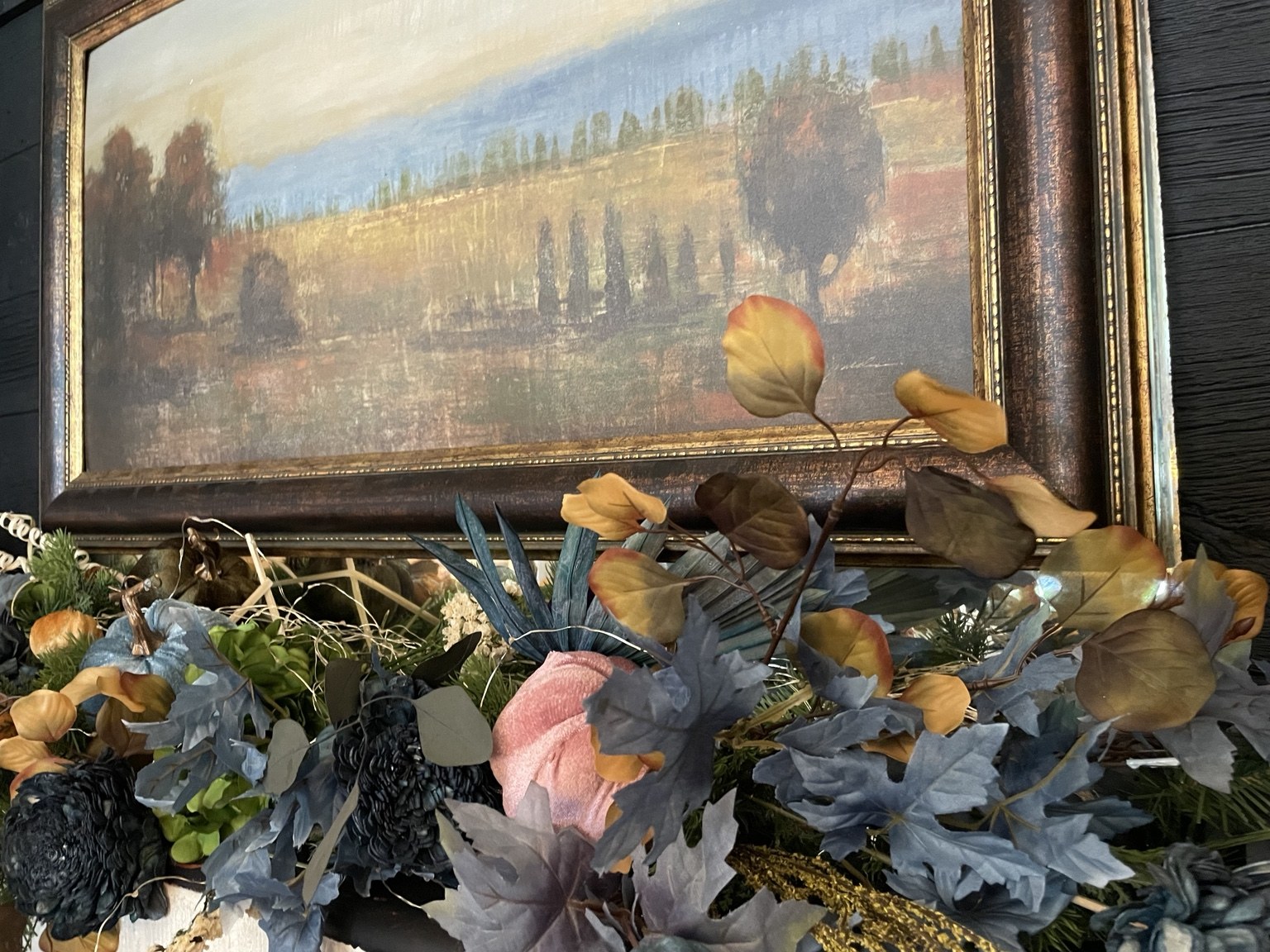 A framed landscape above an arrangement of colorful pumpkins and autumn leaves