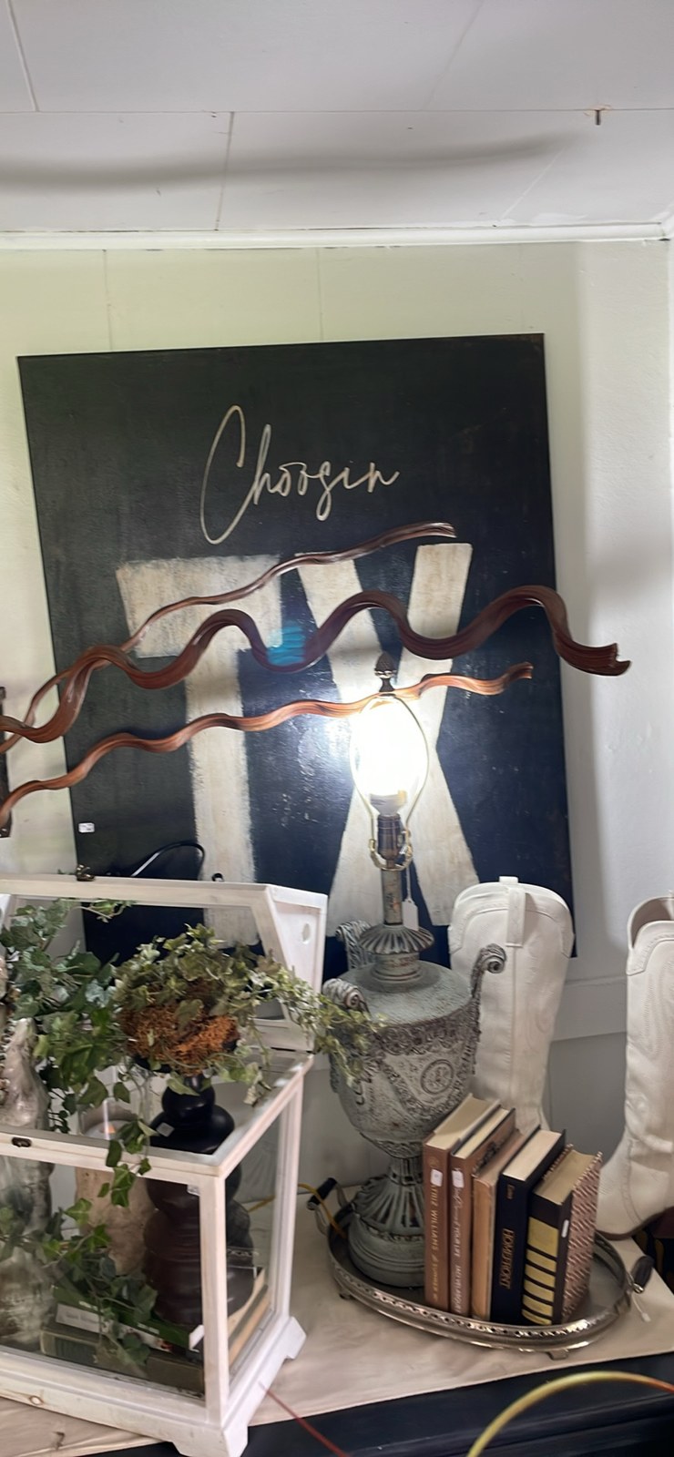An ornate urn lamp, books on a silver tray, greenery, and white cowboy boots